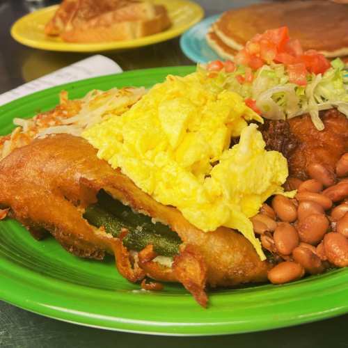 A vibrant plate featuring a stuffed pepper, scrambled eggs, beans, hash browns, and fresh toppings.