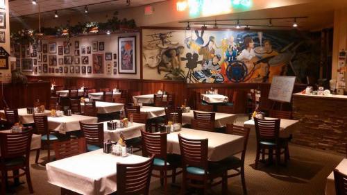A cozy restaurant interior with empty tables, wooden chairs, and a colorful mural on the wall.