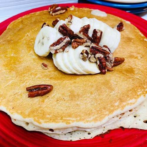 A stack of pancakes topped with sliced bananas and chopped pecans on a red plate.