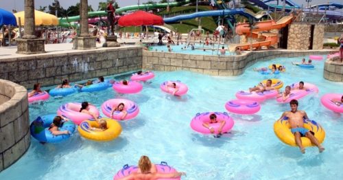 A water park scene with colorful inner tubes floating in a lazy river, surrounded by slides and umbrellas.