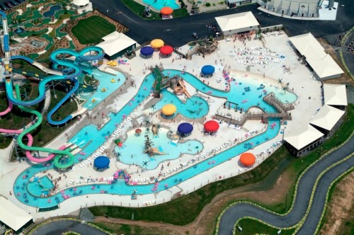 Aerial view of a vibrant water park with pools, slides, and colorful umbrellas, bustling with visitors enjoying the sun.