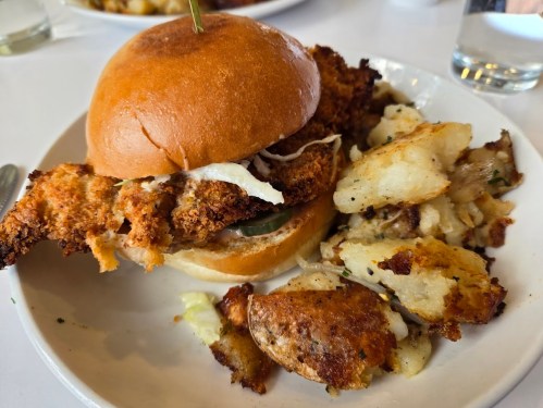 A crispy fried chicken sandwich with pickles and coleslaw, served with seasoned potato wedges on the side.
