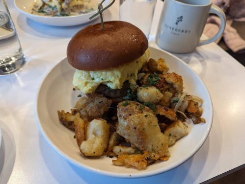A hearty breakfast plate featuring a sandwich with an egg and a side of crispy potatoes and vegetables.