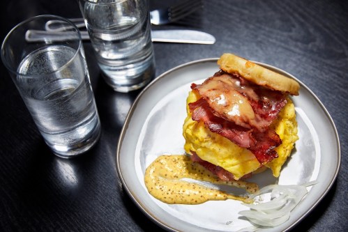 A plate with a sandwich of scrambled eggs, bacon, and sauce, accompanied by two glasses of water.