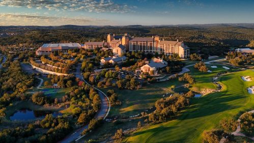Aerial view of a luxury resort surrounded by lush greenery and golf courses under a clear sky.