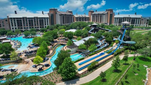 Aerial view of a resort with a large water park, slides, and lush greenery under a blue sky.
