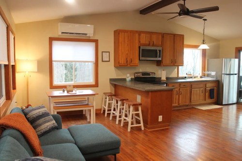 Cozy kitchen and living area with wooden cabinets, a dining table, and a comfortable sofa in a well-lit space.