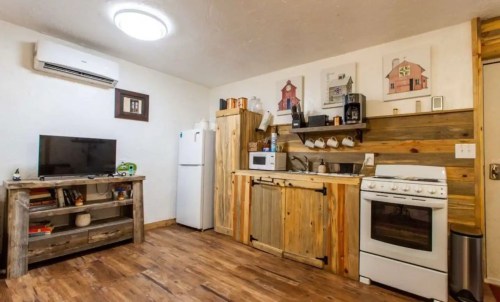 Cozy kitchen with wooden cabinets, white appliances, and a TV, featuring rustic decor and warm lighting.