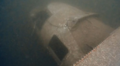 An underwater view of a submerged, rusted object, partially covered in sediment.