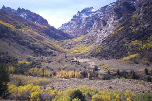 A scenic valley surrounded by mountains, featuring vibrant autumn foliage and a small cabin nestled among the trees.
