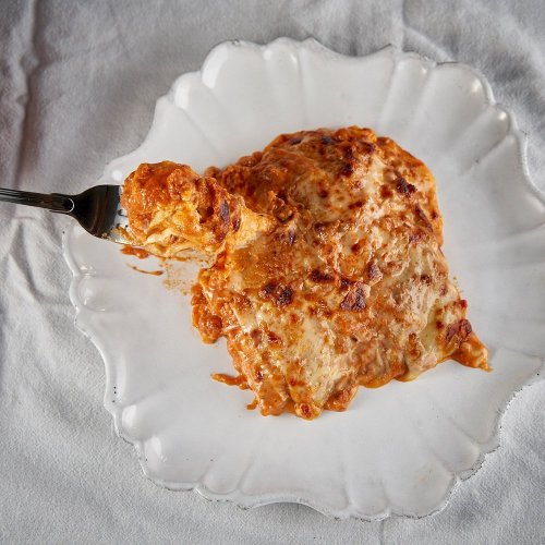 A serving of cheesy lasagna on a decorative white plate, with a fork lifting a piece.