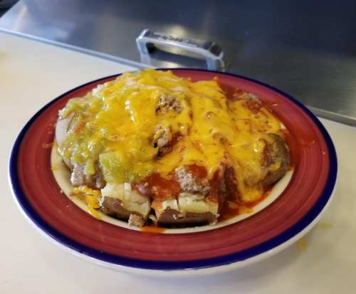 A plate of nachos topped with melted cheese, ground beef, salsa, and green sauce on a bed of tortilla chips.