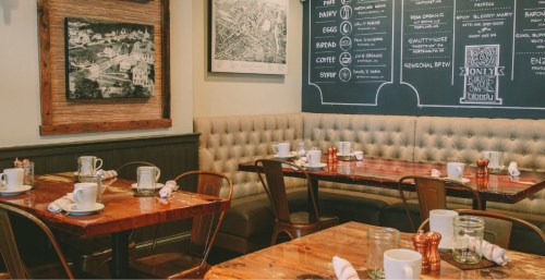 Cozy restaurant interior with wooden tables, chairs, and a chalkboard menu on the wall.