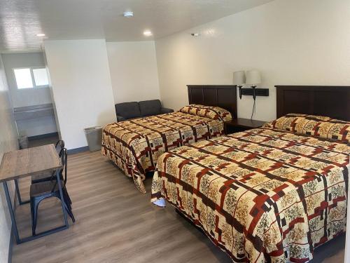 A simple hotel room with two beds, a sofa, a small table, and a closet. The decor features patterned bedspreads.