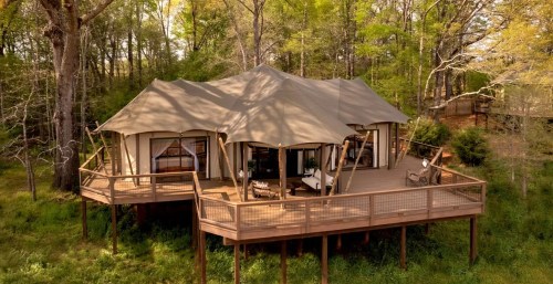 A spacious tent cabin on a wooden deck, surrounded by lush greenery and trees.