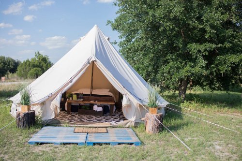 A spacious canvas tent set in a grassy area, featuring a wooden bed and decorative elements outside.