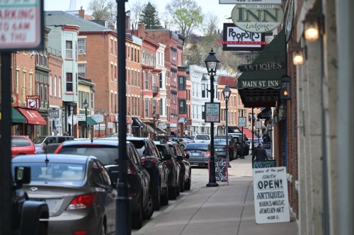 A charming street lined with shops and parked cars, featuring signs for inns and antique stores.