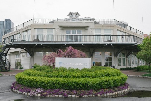 A waterfront building with a sign reading "Maritime Parc," surrounded by greenery and blooming flowers.