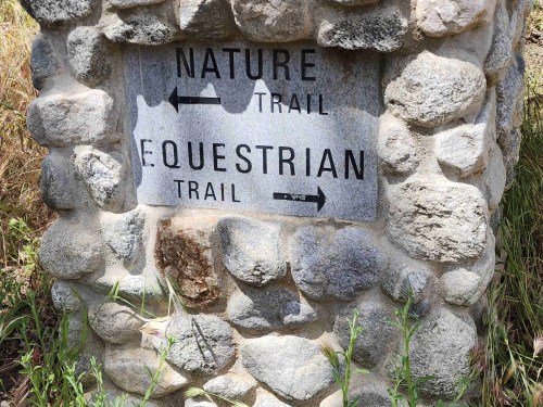 Signpost with stone base indicating directions for Nature Trail and Equestrian Trail, with arrows pointing left and right.