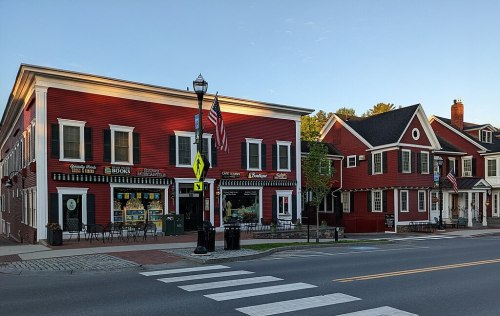 A charming street view of red buildings with flags, featuring a bookstore and outdoor seating, under a clear blue sky.
