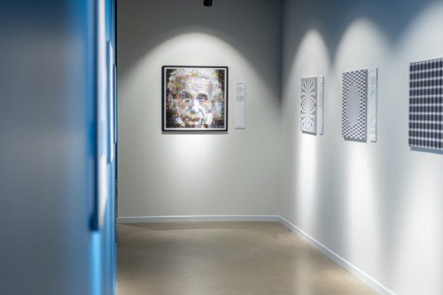 A gallery hallway featuring a prominent artwork of a face, surrounded by geometric patterns on the walls.