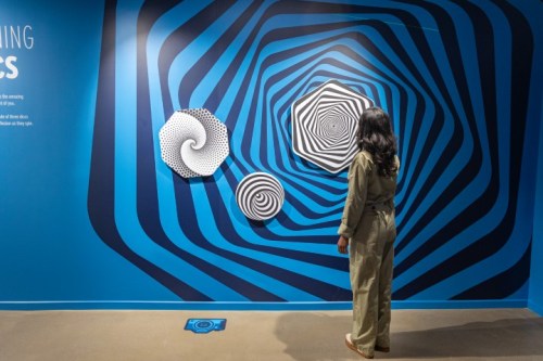 A person stands in front of spiral-patterned art on a blue wall, creating a sense of depth and movement.