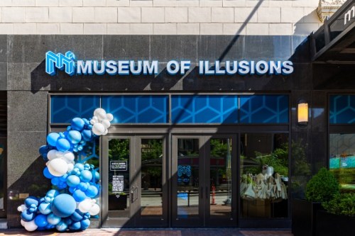 Entrance of the Museum of Illusions, featuring a blue and white balloon arch and modern signage.