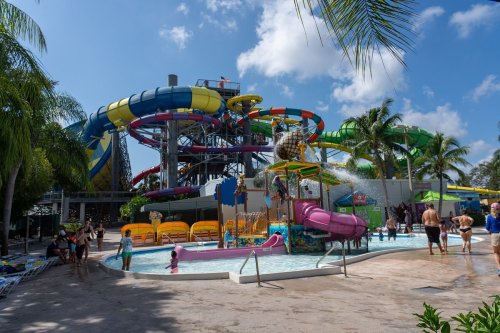 A vibrant water park featuring colorful slides, a splash area, and families enjoying the sunny day.