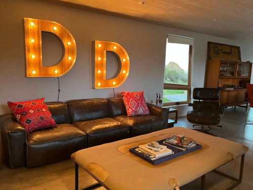 Cozy living room with a leather sofa, decorative pillows, a coffee table, and illuminated letter signs on the wall.