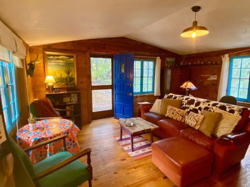 Cozy cabin interior with wooden walls, blue door, comfortable seating, and colorful decor. Warm, inviting atmosphere.
