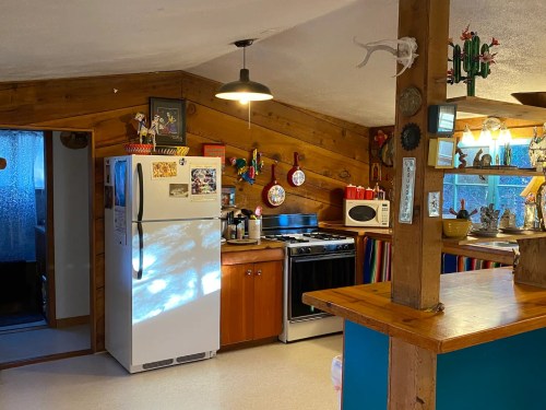 Cozy kitchen with wooden walls, a white fridge, stove, and colorful decor, featuring a warm, inviting atmosphere.