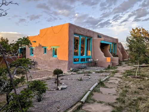 A colorful adobe-style house with turquoise accents, surrounded by a landscaped garden and stone pathway.