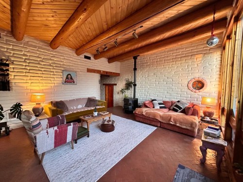 Cozy living room with wooden beams, colorful sofas, a rug, and a wood stove, featuring warm lighting and decorative accents.