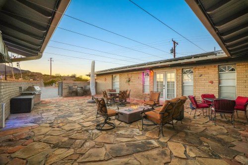 Cozy outdoor patio with stone flooring, seating, and a fire pit, surrounded by a desert landscape at sunset.
