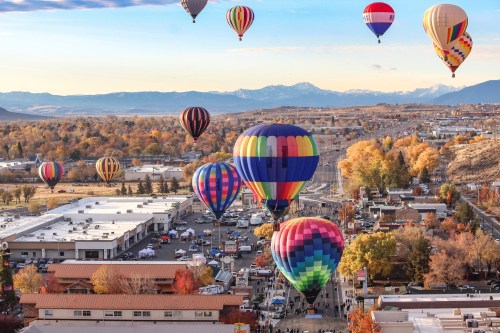 A vibrant scene of colorful hot air balloons floating over a town with autumn trees and mountains in the background.