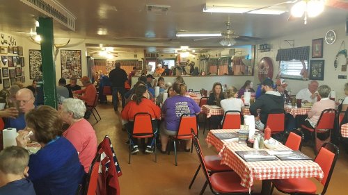 A busy diner with red-checkered tables, filled with people enjoying meals and chatting in a cozy atmosphere.