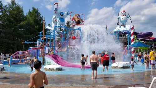 A vibrant water park scene with kids playing, water slides, and a large splash area under a sunny sky.