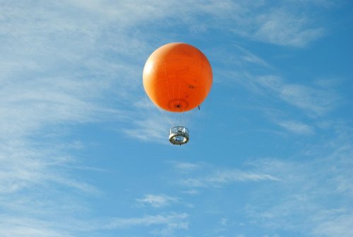 An orange hot air balloon floats against a blue sky with wispy clouds.