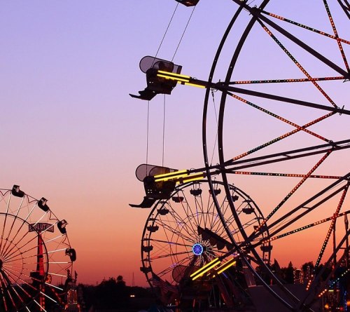 Silhouettes of ferris wheels against a colorful sunset sky.