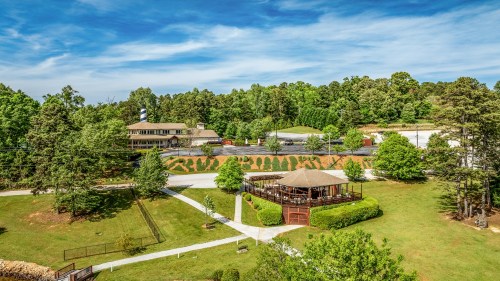 A scenic view of a landscaped area with a gazebo, surrounded by trees and a building in the background under a blue sky.