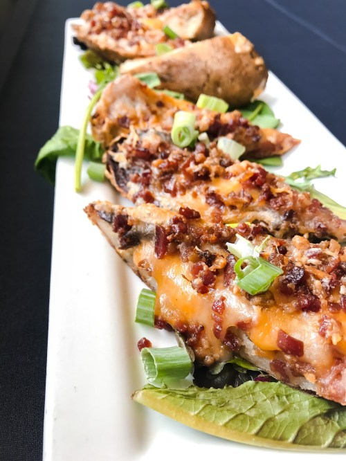 A platter of baked potatoes topped with cheese, bacon bits, and green onions, served on a bed of lettuce.
