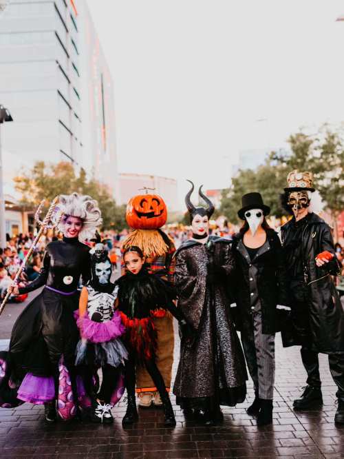 A group of people in Halloween costumes, including a witch, pumpkin, and various spooky characters, posing together.