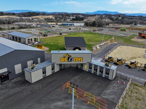 Aerial view of Dig In Zone, featuring buildings, machinery, and a large outdoor area with mountains in the background.