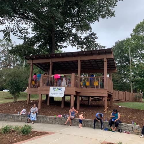 A wooden pavilion with colorful chairs, surrounded by trees, where people relax and socialize in a park setting.
