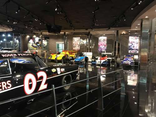 A sleek car showroom featuring various race cars displayed under bright lights and modern decor.