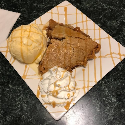 A slice of pie with a scoop of vanilla ice cream, topped with whipped cream and drizzled with caramel sauce.