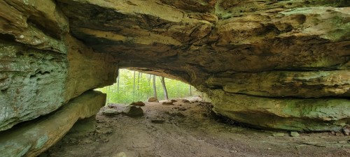 A natural rock formation with an archway, leading to a lush green forest in the background.
