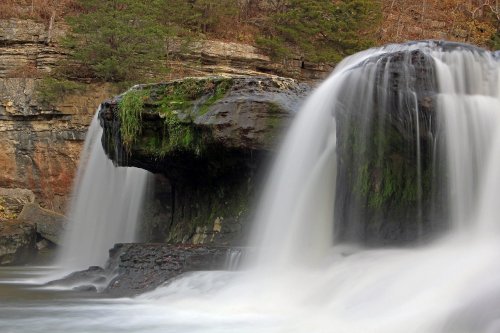 A serene waterfall cascades over a rocky ledge, surrounded by lush greenery and rugged cliffs.