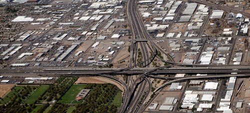 Aerial view of a highway interchange surrounded by industrial buildings and green spaces.