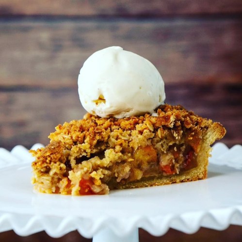 A slice of pie topped with a scoop of vanilla ice cream on a decorative white plate.